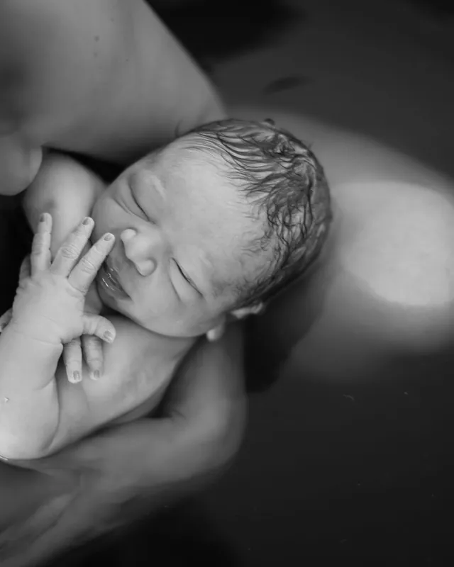 A newborn's first minutes, held close in the water, black and white birth photography by Jenn Miller, Orange County