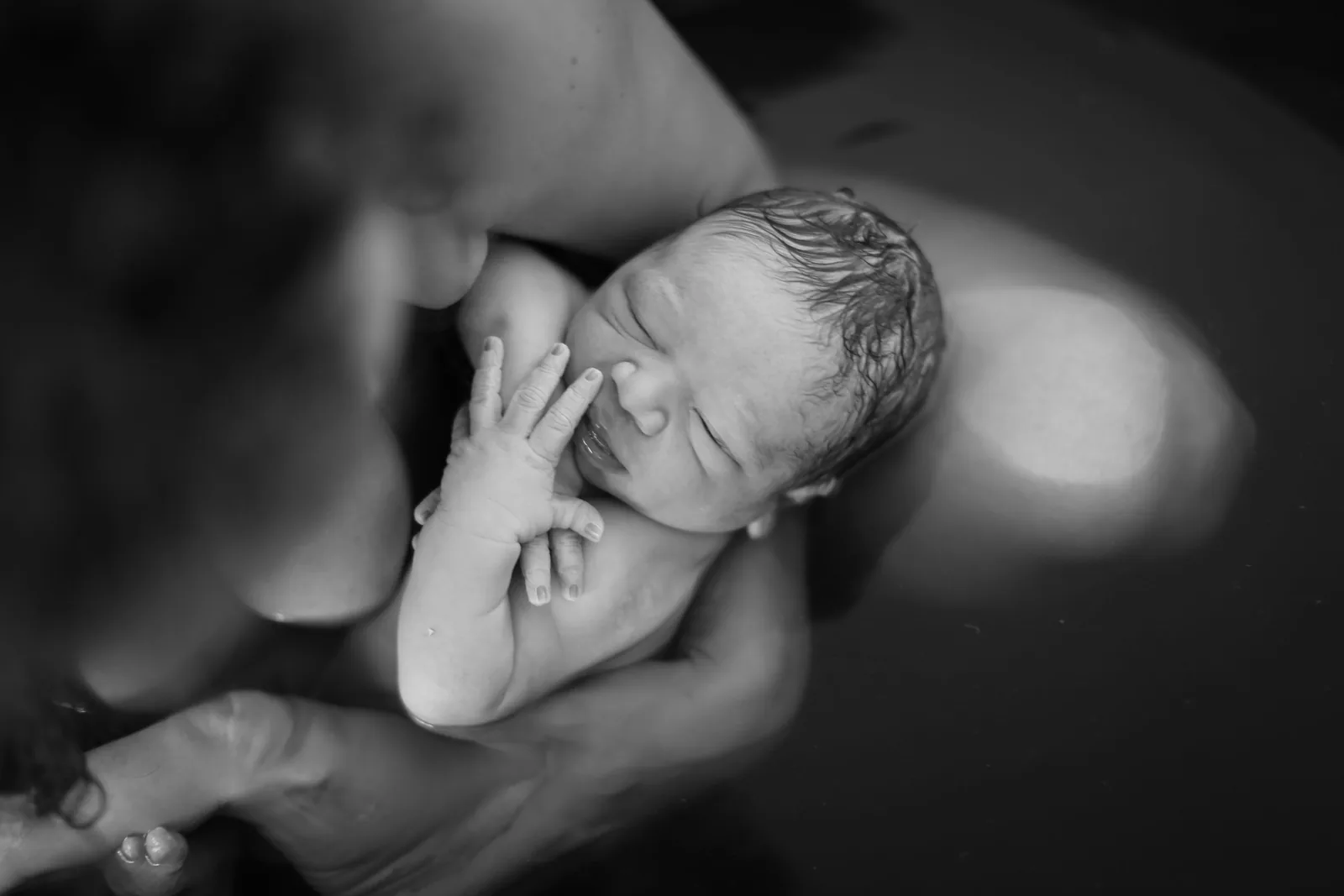 A newborn's first minutes, held close in the water, black and white birth photography by Jenn Miller