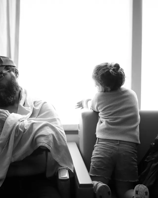 A father holds his newborn by the window while big sister looks out, black and white birth photography by Jenn Miller, Orange County