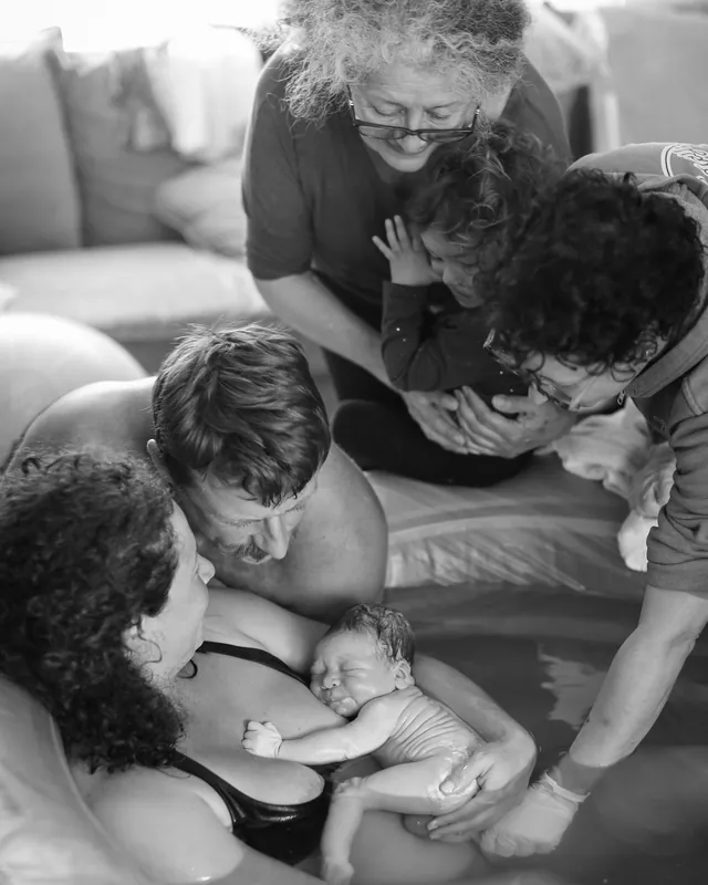 Family gathers around the birth pool to meet the baby, black and white birth photography by Jenn Miller, Orange County