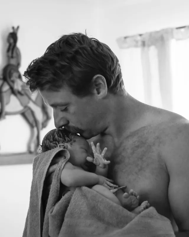 A father kisses his newborn's head, black and white birth photography by Jenn Miller, Orange County