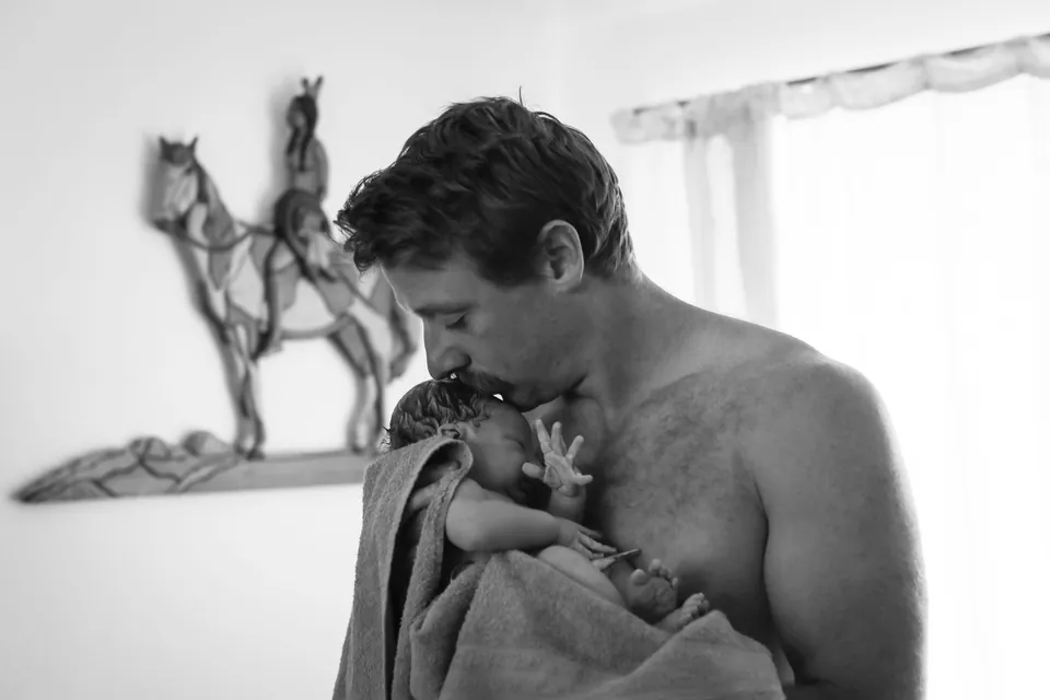 A father kisses his newborn's head, black and white birth photography by Jenn Miller