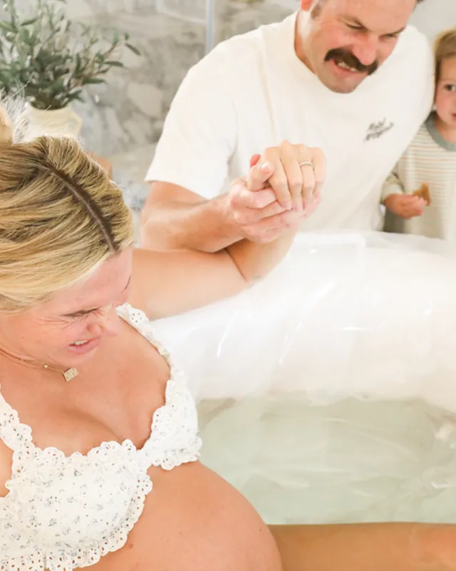 A laboring mother holds her partner's hand in the birth tub while their toddler watches, Orange County birth photography by Jenn Miller