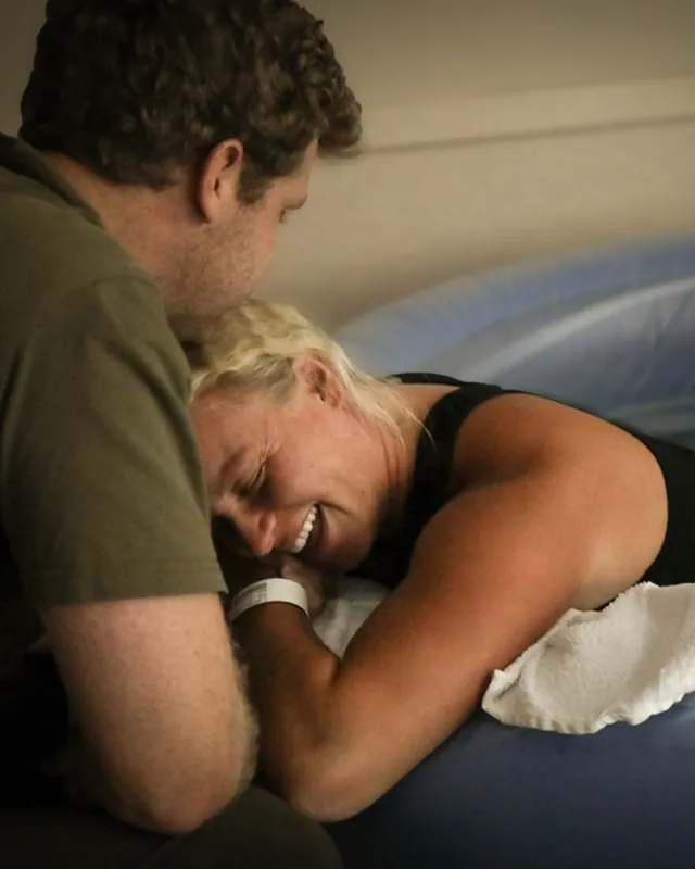A laboring mother leans on her partner beside the birth pool, Orange County birth photography by Jenn Miller