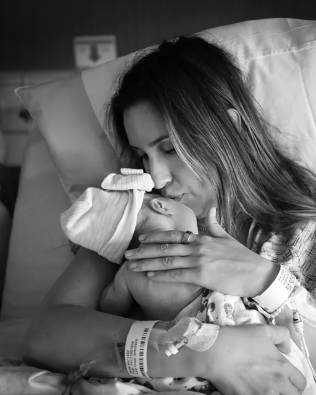 A mother kisses her newborn's head, black and white birth photography by Jenn Miller, Orange County