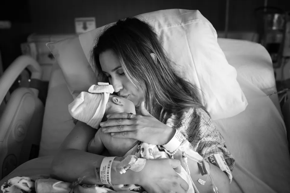 A mother kisses her newborn's head, black and white birth photography by Jenn Miller