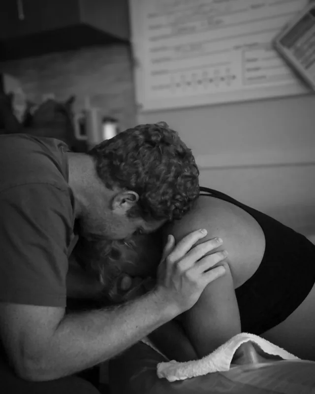 A partner holds a laboring mother close, black and white birth photography by Jenn Miller, Orange County
