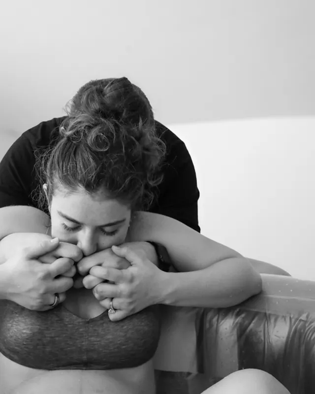 A laboring mother grips her partner's hands at the birth pool, black and white birth photography by Jenn Miller, Orange County