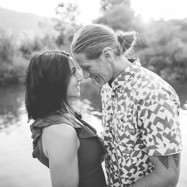Jenn Miller and her husband smiling forehead to forehead beside the water, in black and white