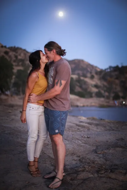 Jenn Miller and her husband kissing on a rocky shore under the moon