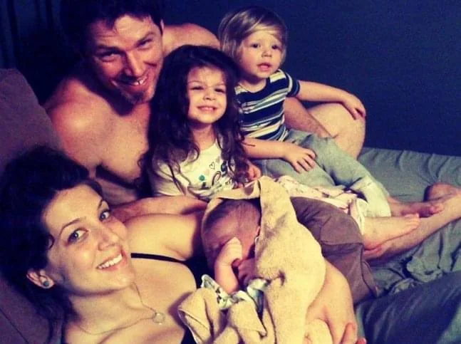Jenn Miller in bed just after giving birth, her newborn on her chest and her husband and two children leaning in