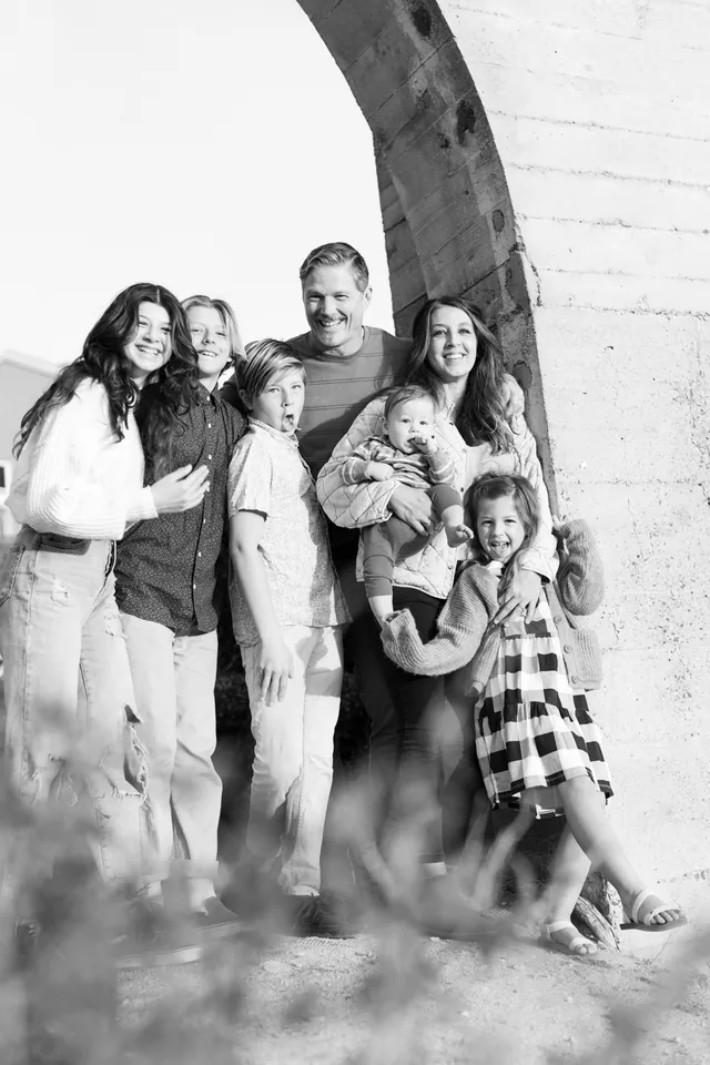 Jenn Miller, her husband and their five children laughing beside a stone arch, in black and white