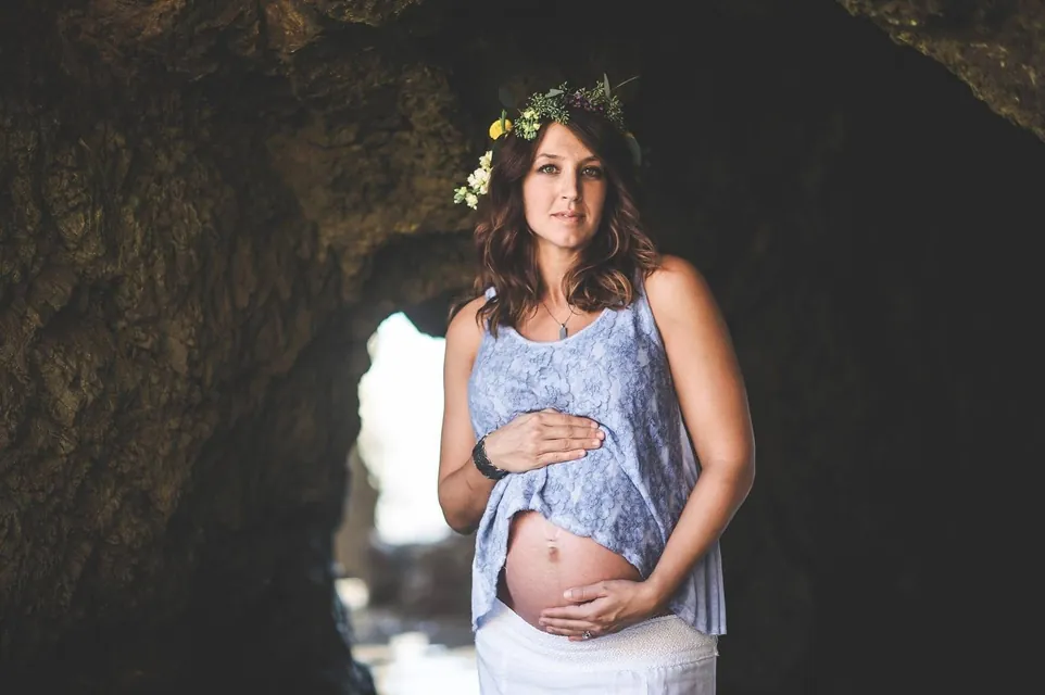 Jenn Miller, pregnant, wearing a flower crown and cradling her belly inside a sea cave
